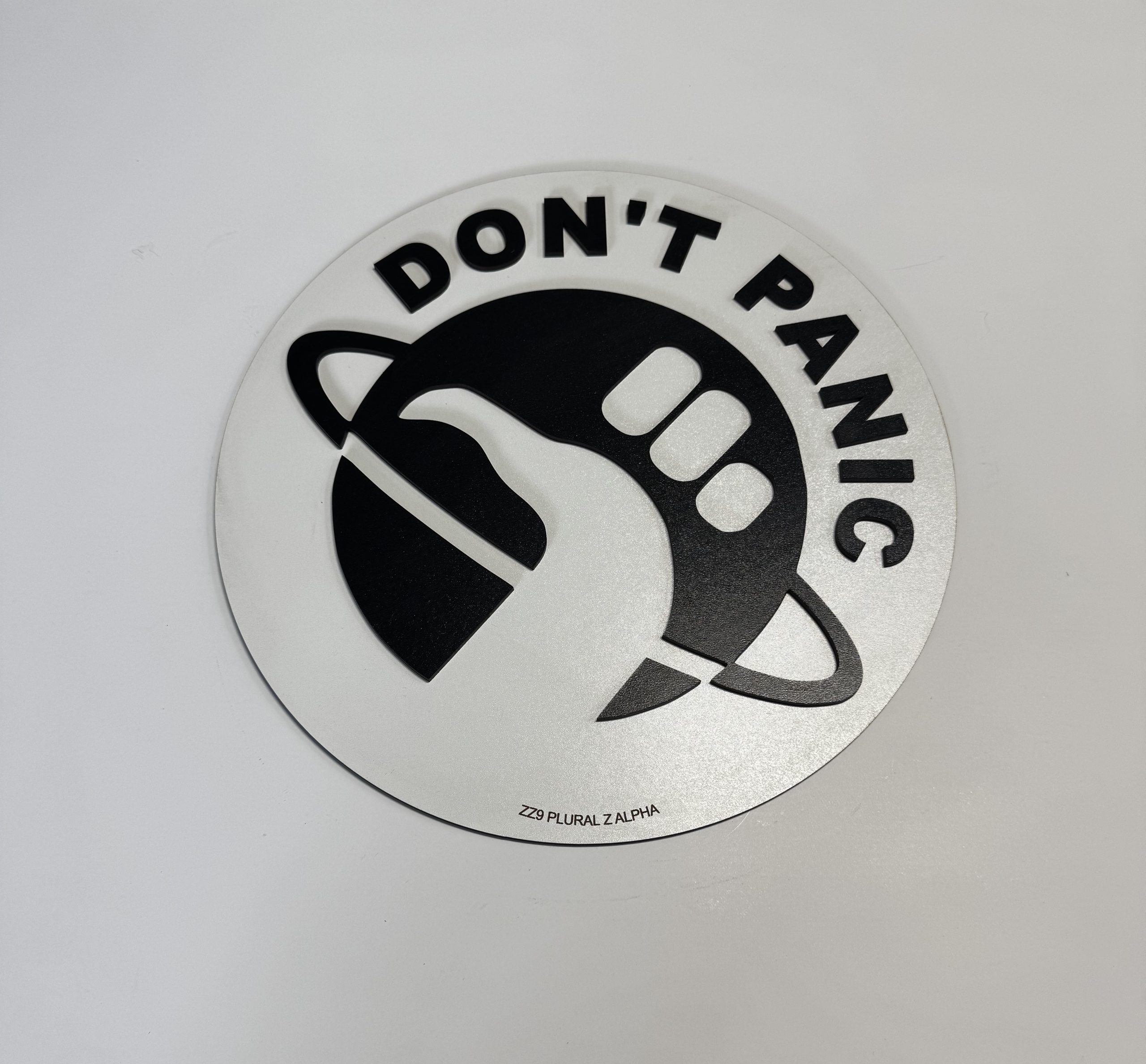 Circular black‑and‑white emblem featuring “DON’T PANIC” text and a stylised hand giving a thumbs‑up over a ringed planet, designed by Boon Hill Designs.