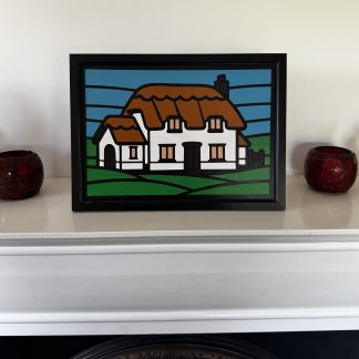 Stylised faux stained‑glass A4 MDF panel depicting a cottage with thatched roof, white walls, and geometric sky and field shapes.”