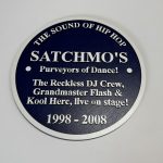 Hip-hop commemorative plaque featuring Satchmo’s, Grandmaster Flash and Kool Herc in white text on a dark blue circular design.