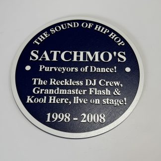 Hip-hop commemorative plaque featuring Satchmo’s, Grandmaster Flash and Kool Herc in white text on a dark blue circular design.